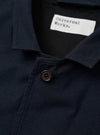The Navy Valencia Cotton Two Button Jacket is shown from the back as a flat lay against a plain white background. The image highlights the clean construction of the garment's rear, featuring two side vents at the hem and a two-piece sleeve design. The fabric is a dark navy blue with a smooth finish.