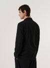 A model wears the Black Valencia Cotton Two Button Jacket, shown from the back against a plain white background. The jacket features a structured silhouette with a clean back panel and a central vent at the hem. The black fabric, a blend containing recycled cotton, has a smooth and uniform appearance. The model is standing facing away from the camera.
