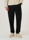 A model wears the Black Valencia Cotton Military Chino while standing against a plain white background. The trousers feature a straight-leg fit, front slash pockets, and a structured waistband with belt loops. The black fabric has a smooth, durable finish characteristic of the Valencia cotton blend. The model is shown from the waist down, highlighting the garment's classic military-inspired silhouette and clean construction.