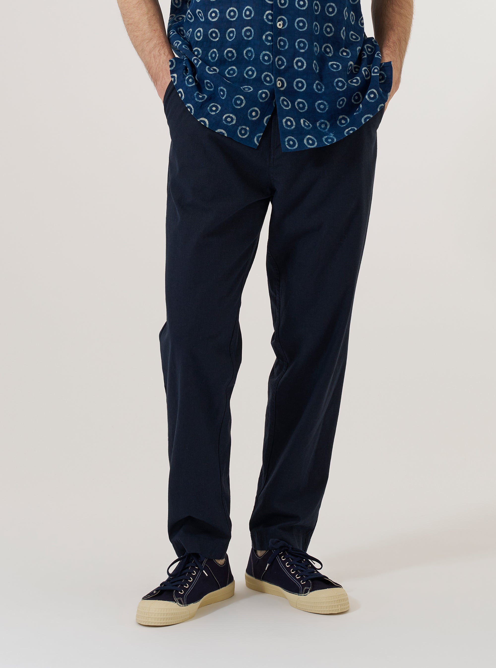 A model wears the Navy Valencia Cotton Military Chino, shown from the waist down against a plain white background. The trousers feature a regular fit with a tapered leg, two front pockets, and a visible button fly. The fabric is a dark navy blue with a subtle textured finish. The model is also wearing a light-colored long-sleeve shirt and dark shoes.