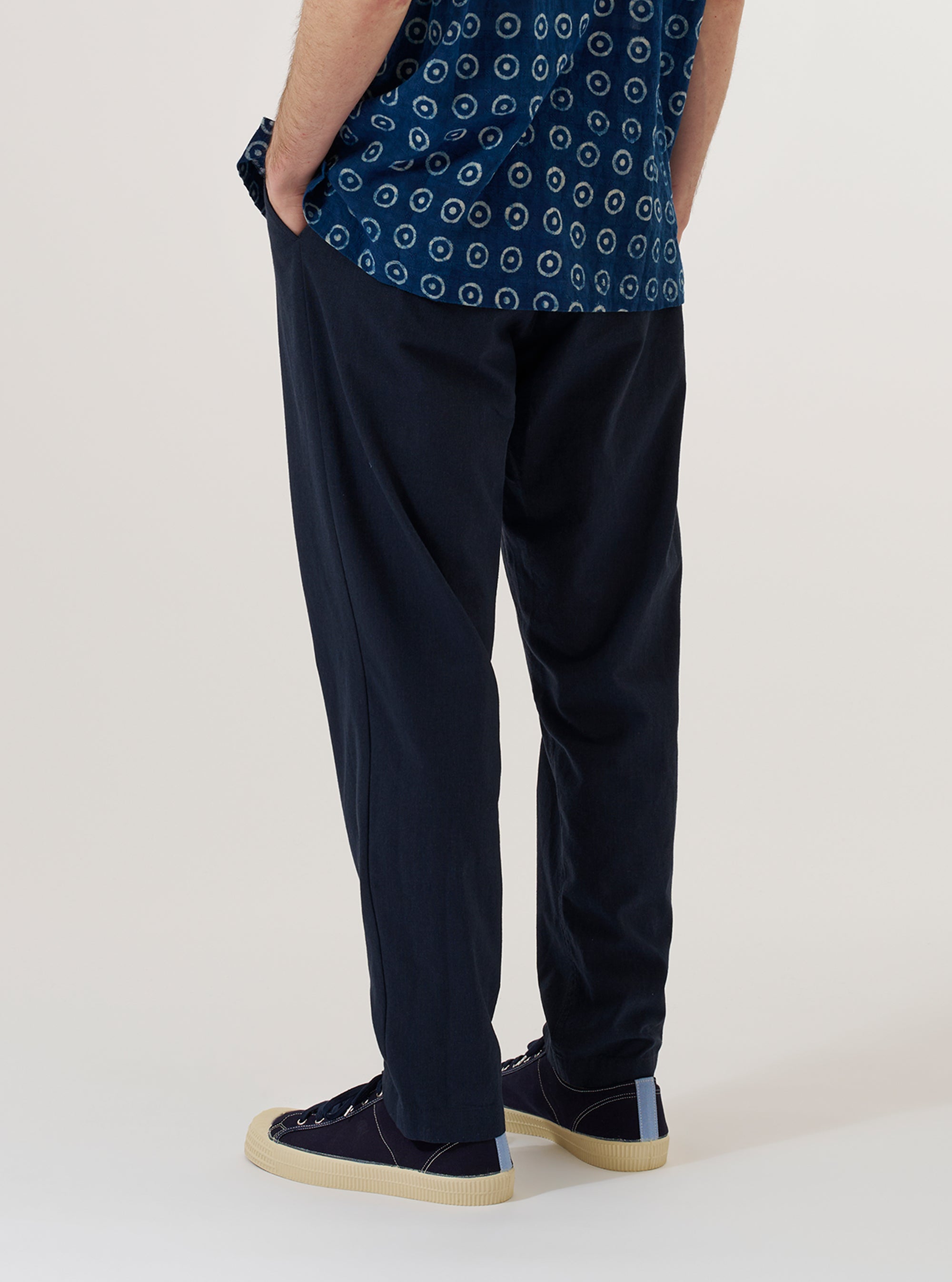 A model wears the Navy Valencia Cotton Military Chino, shown from the back against a plain white background. The image highlights the straight-leg fit and the two rear pockets, one of which features a button-down flap. The textured navy cotton fabric and the clean finish of the hem are clearly visible.