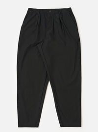 The Black Valencia Cotton Pleated Track Pant is shown as a flat lay against a white background. The trousers feature a loose, tapered leg with a single pleat at the front and an elasticated drawstring waistband. The fabric is a smooth black cotton blend.