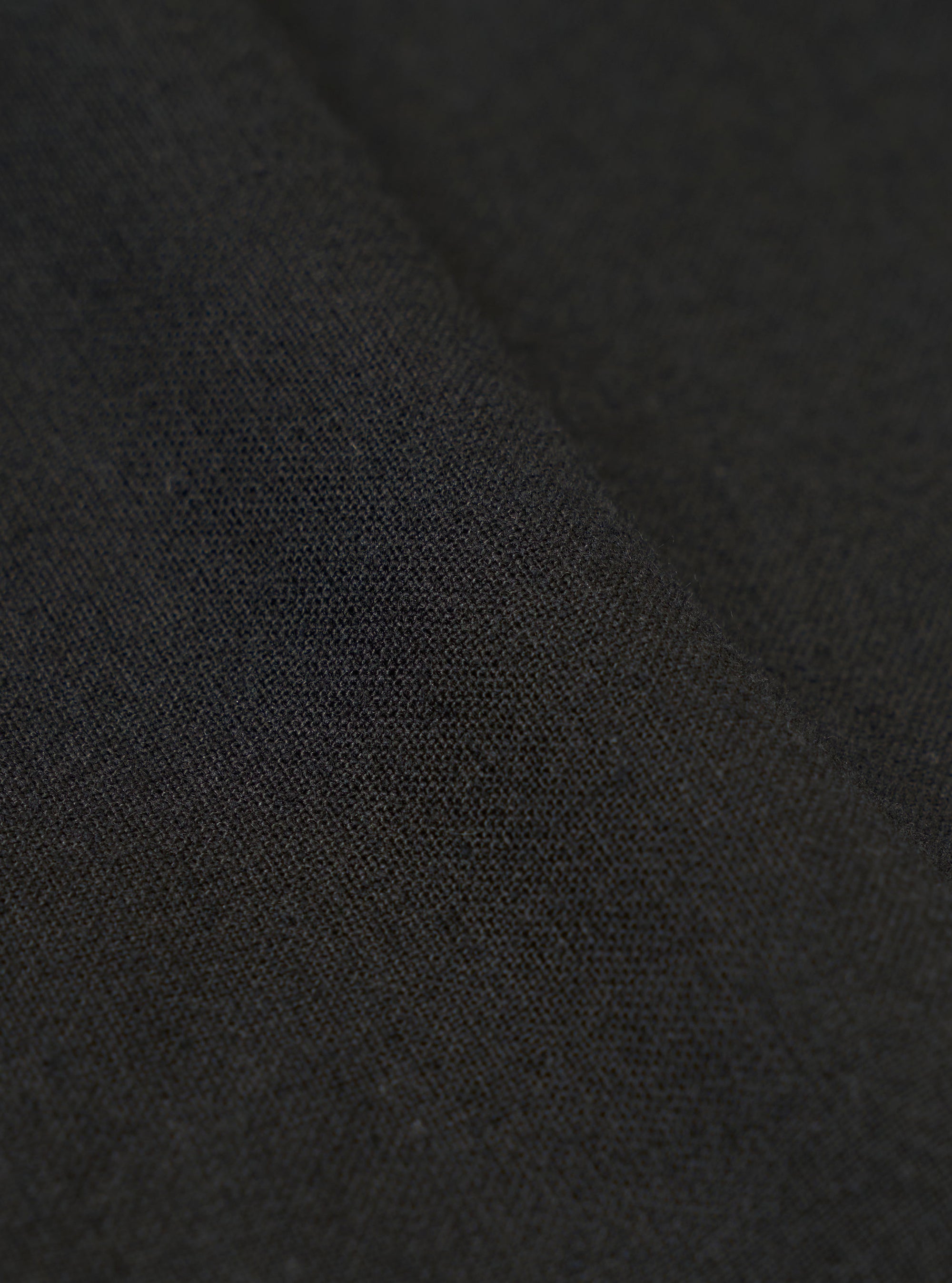 A close-up swatch image of the Black Valencia Cotton Pleated Track Pant fabric highlights the fine, plain weave and smooth texture of the black material. The fabric fills the entire frame, providing a detailed view of the lightweight suiting blend.