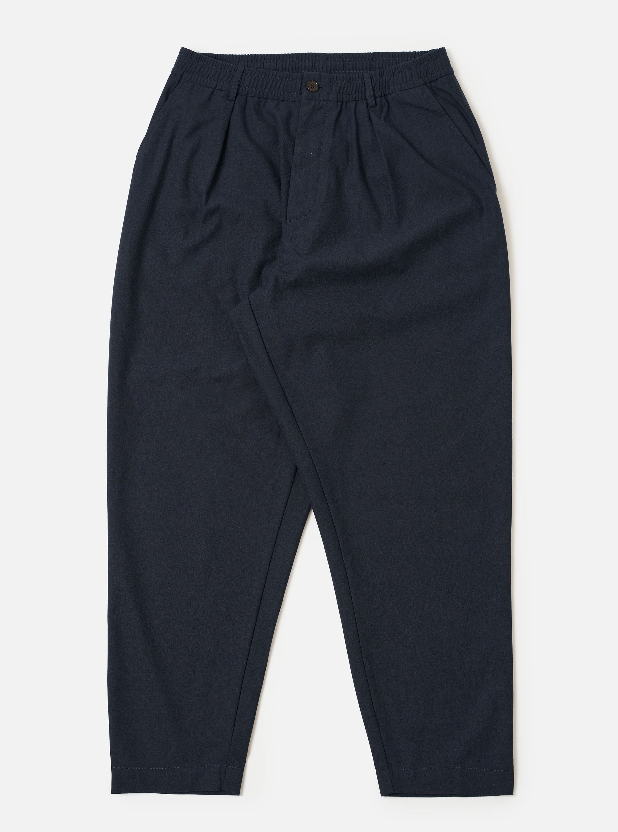 The Navy Valencia Cotton Pleated Track Pant is shown as a flat lay against a plain white background. The trousers feature an elasticated waistband with an external drawstring, a single pleat at the front, and two side pockets. The fabric is a dark navy blue with a smooth, clean finish.