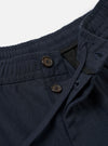 The Navy Valencia Cotton Pleated Track Pant is shown from the back as a flat lay against a plain white background. The image highlights the two rear pockets, including one with a buttoned flap and one jetted pocket, as well as the elasticated waistband and the tapered leg construction.