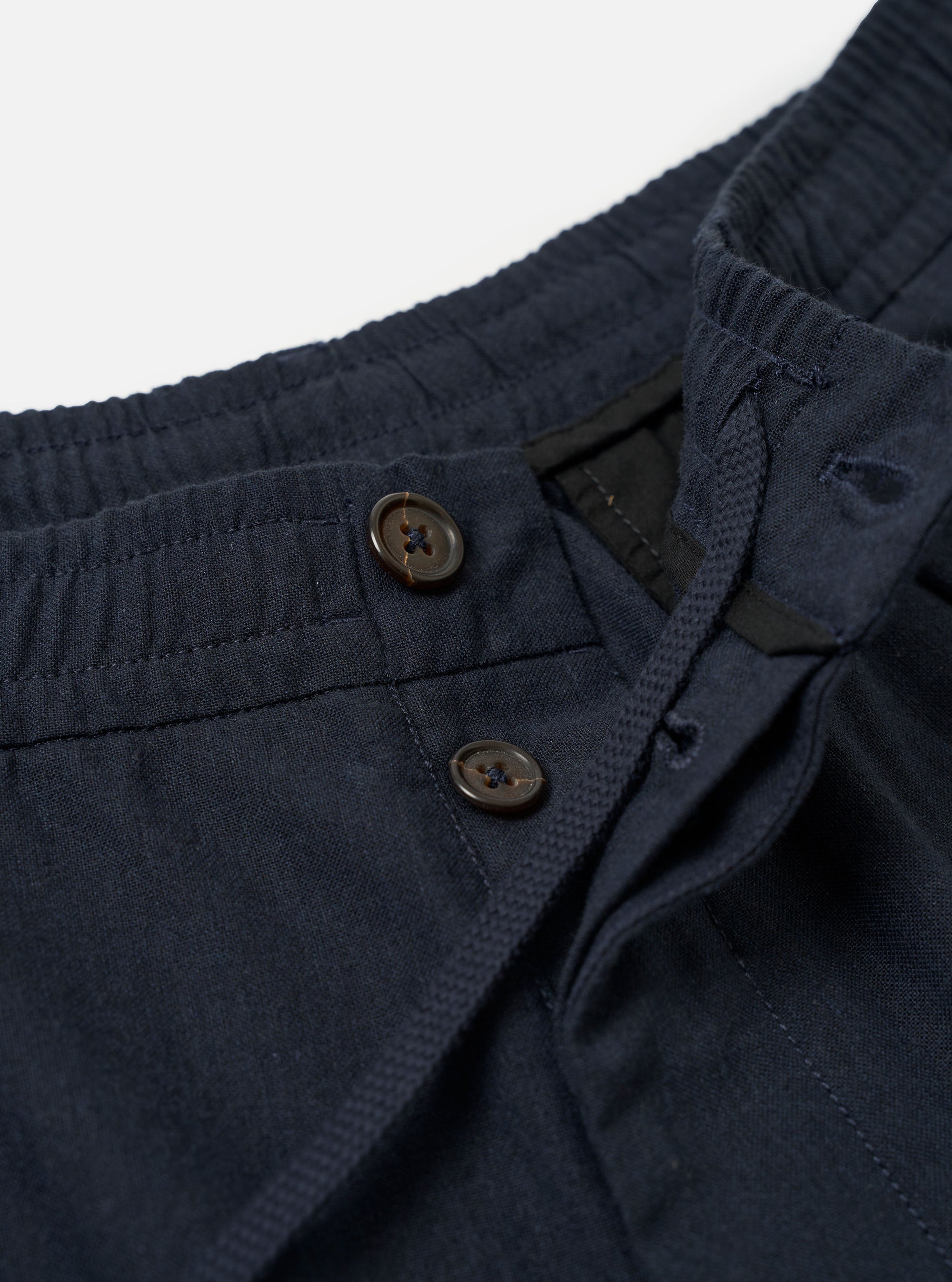 The Navy Valencia Cotton Pleated Track Pant is shown from the back as a flat lay against a plain white background. The image highlights the two rear pockets, including one with a buttoned flap and one jetted pocket, as well as the elasticated waistband and the tapered leg construction.
