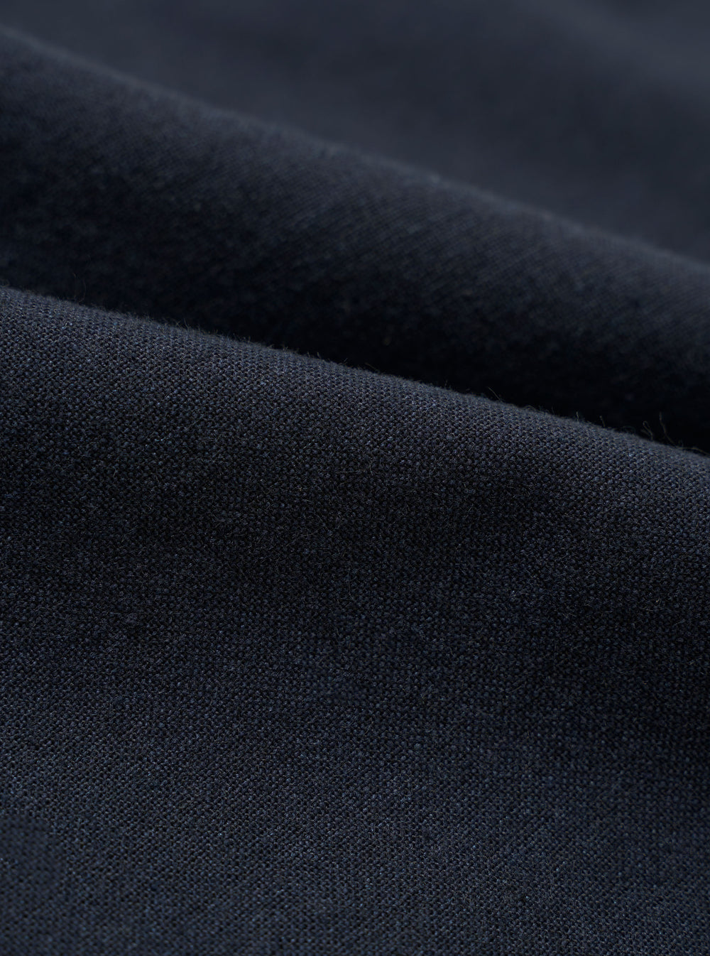 A close-up swatch image of the Navy Valencia Cotton Pleated Track Pant fabric. The image focuses on the textile detail, showing a deep navy blue color with a fine, clean, plain weave texture.