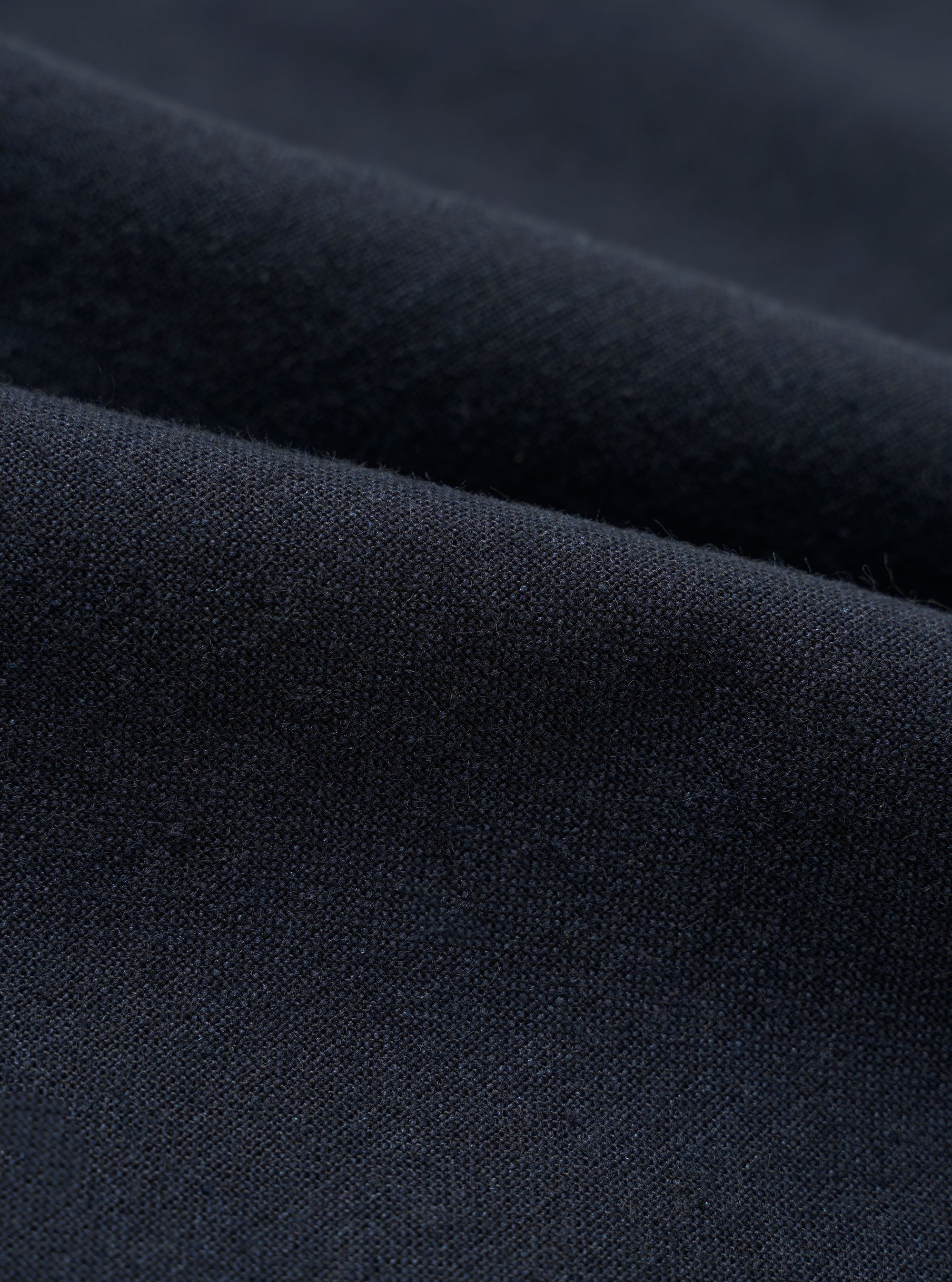 A close-up swatch image of the Navy Valencia Cotton Pleated Track Pant fabric. The image focuses on the textile detail, showing a deep navy blue color with a fine, clean, plain weave texture.