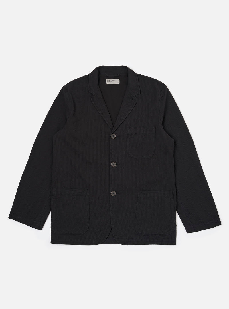 The Black Merida Seersucker Three Button Jacket is shown as a flat lay against a white background. This loose-fitting, unstructured jacket features three front buttons, a single chest patch pocket, and two lower patch pockets. The black cotton fabric has a distinct puckered seersucker texture.