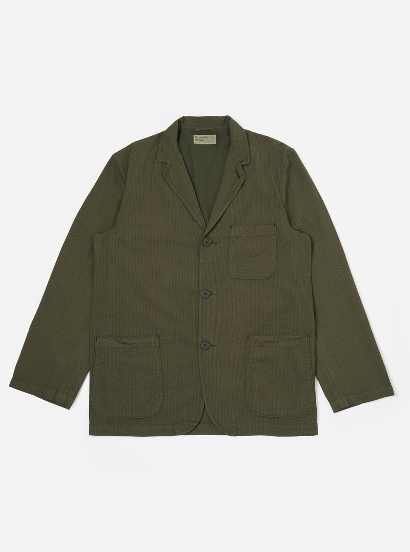 The Olive Merida Seersucker Three Button Jacket is shown as a flat lay against a white background. The jacket features a three-button front closure, a notched lapel with a button hole, one chest patch pocket, and two larger lower patch pockets. The olive green fabric has a distinct puckered seersucker texture.