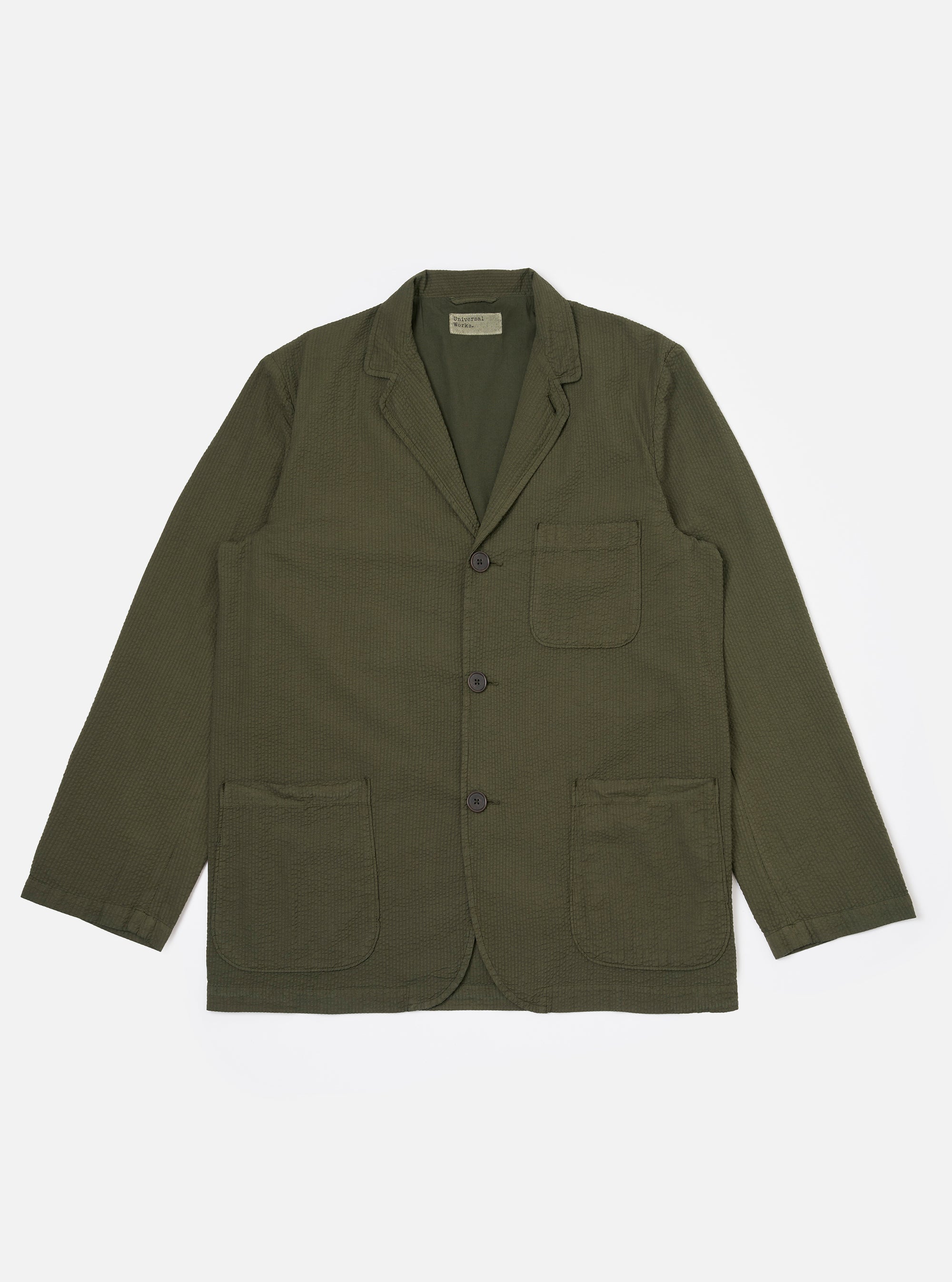 The Olive Merida Seersucker Three Button Jacket is shown as a flat lay against a white background. The jacket features a three-button front closure, a notched lapel with a button hole, one chest patch pocket, and two larger lower patch pockets. The olive green fabric has a distinct puckered seersucker texture.