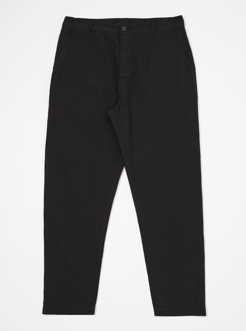 The Black Merida Seersucker Military Chino is shown as a flat lay against a white background. The trousers feature a high rise with a one-piece Hollywood waistband, slash front pockets, and a buttoned fly. The fabric has a distinct black puckered seersucker texture.