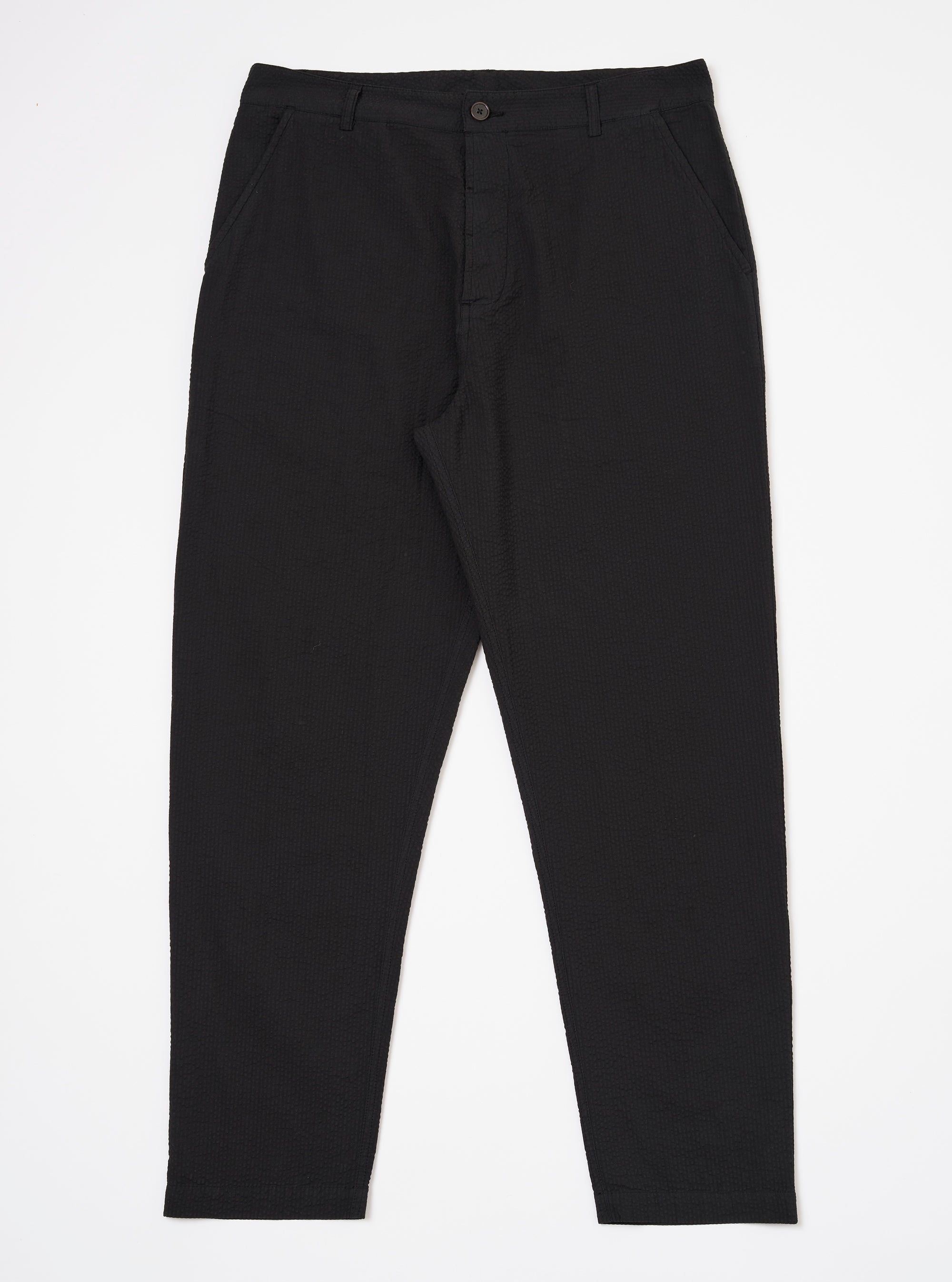 The Black Merida Seersucker Military Chino is shown as a flat lay against a white background. The trousers feature a high rise with a one-piece Hollywood waistband, slash front pockets, and a buttoned fly. The fabric has a distinct black puckered seersucker texture.