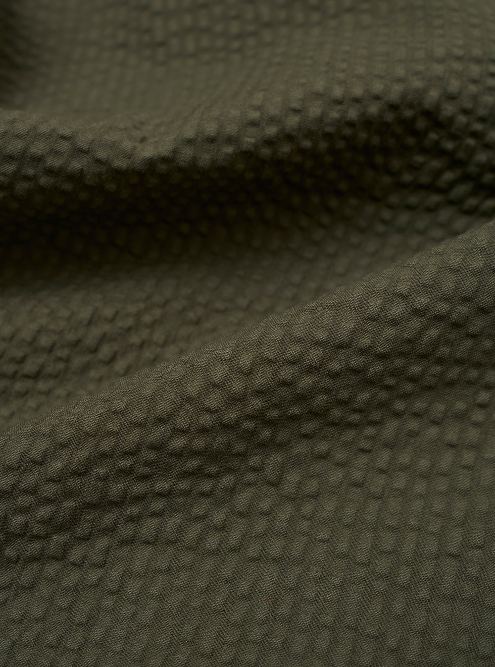 A close-up swatch image of the Olive Merida Seersucker Military Chino fabric highlights the olive green color and the characteristic puckered texture of the cotton seersucker material.