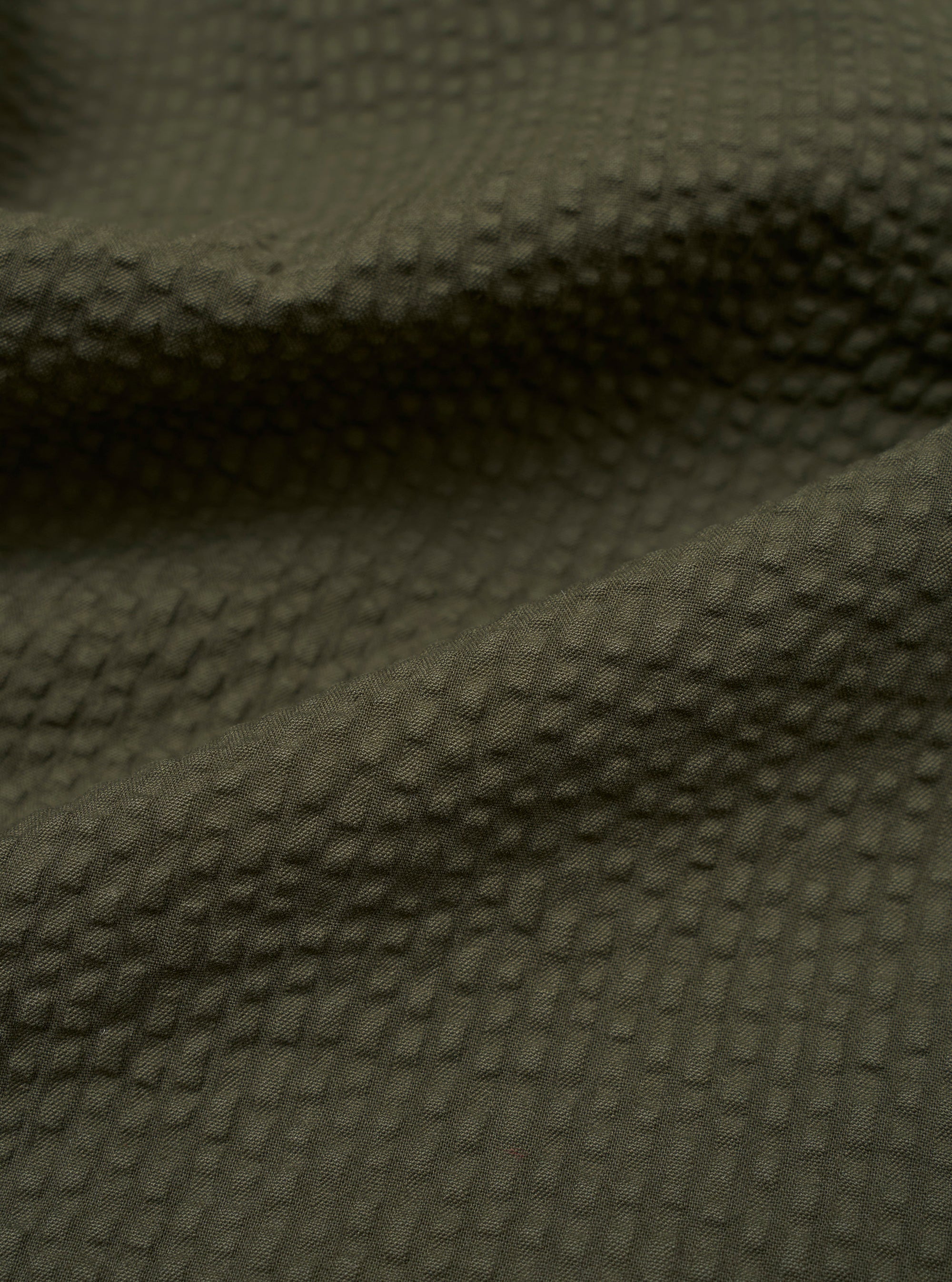 A close-up swatch image of the Olive Merida Seersucker Military Chino fabric highlights the olive green color and the characteristic puckered texture of the cotton seersucker material.