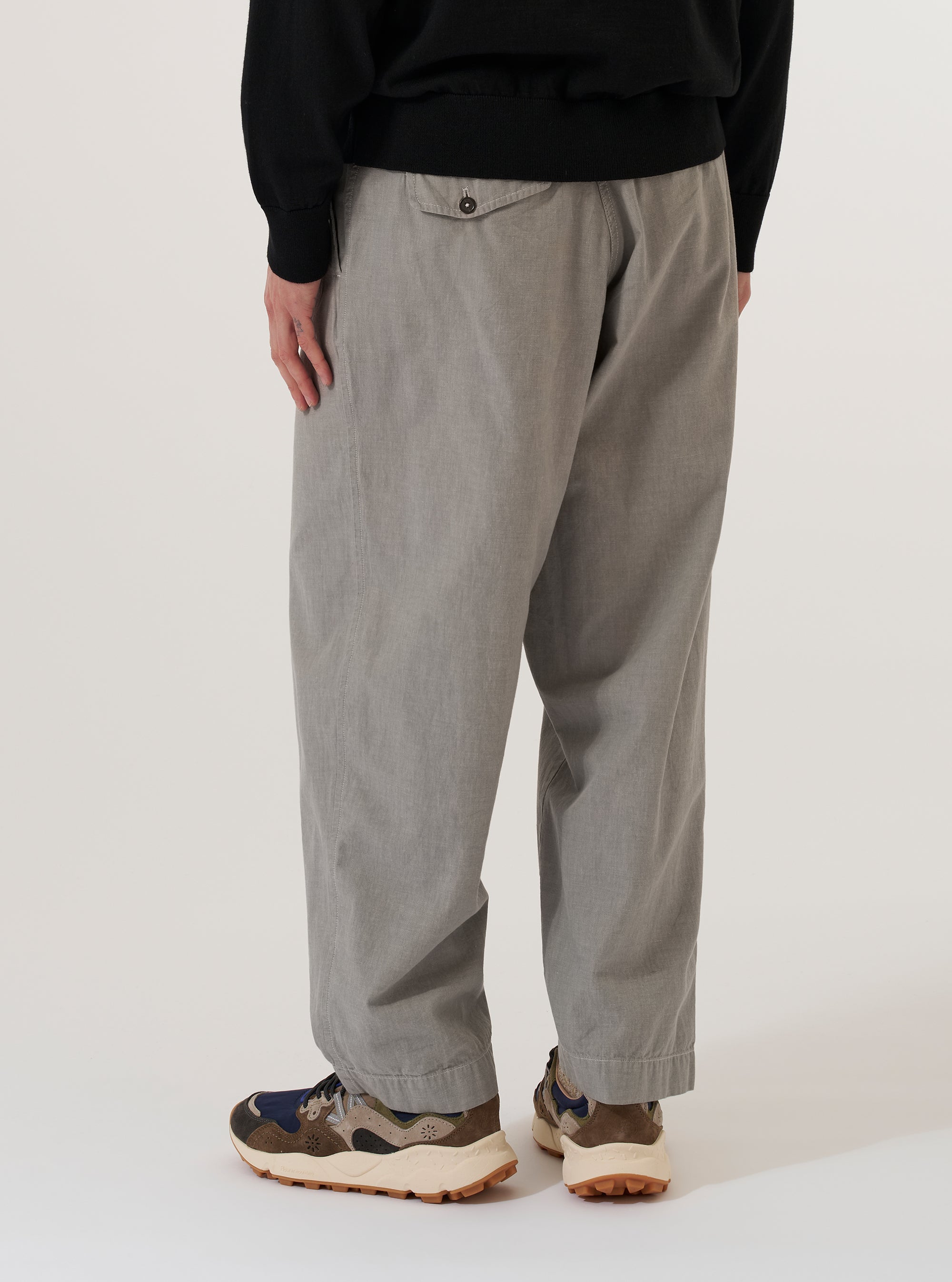 A model wears the Grey Izumi Cotton Oxford Pant against a plain white background. Shown from the waist down, the trousers feature a loose, wide-leg fit and a pleated front. The grey Izumi cotton fabric is detailed with a drawstring at the waist and functional side pockets.