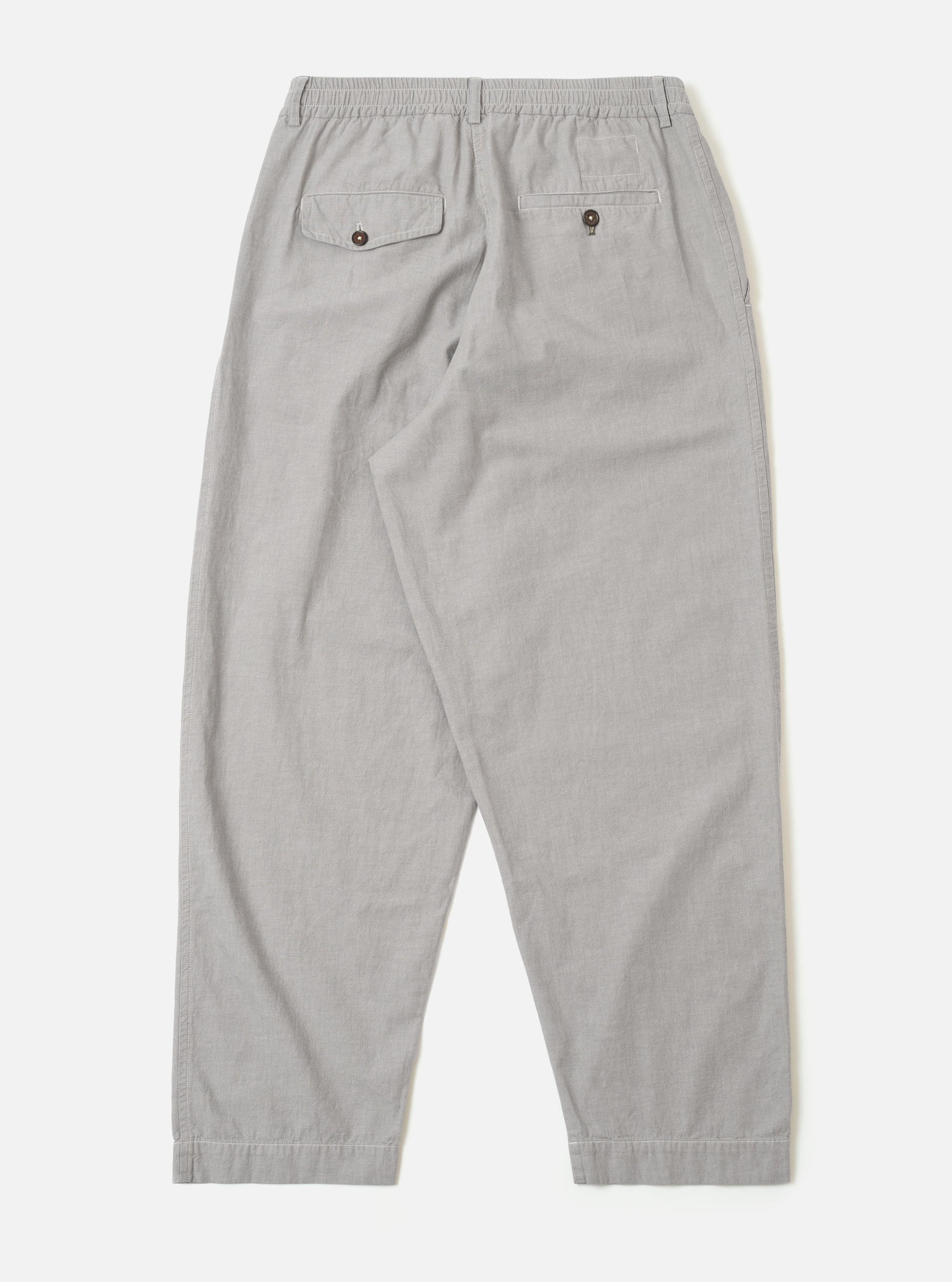 The Grey Izumi Cotton Oxford Pant is shown from the back as a flat lay against a plain white background. The image highlights the two rear pockets, including one with a buttoned flap and one buttoned jetted pocket, as well as the elasticated drawstring waistband. The grey cotton fabric features a subtle textured weave.