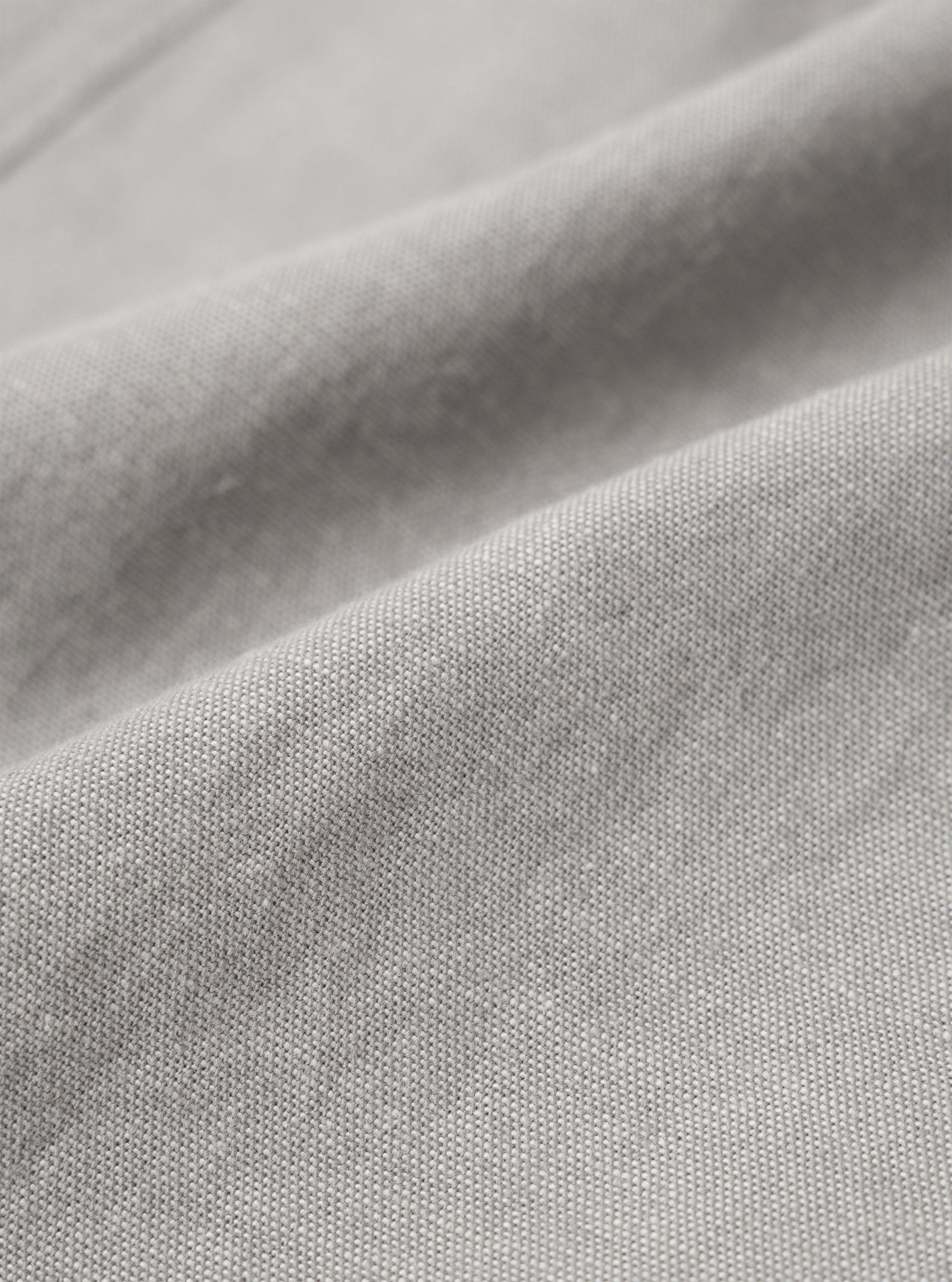 A close-up fabric swatch of the Grey Izumi Cotton Hi Water Trouser highlights the material's color and texture. The image shows a grey cotton fabric with a subtle, fine-grained weave.