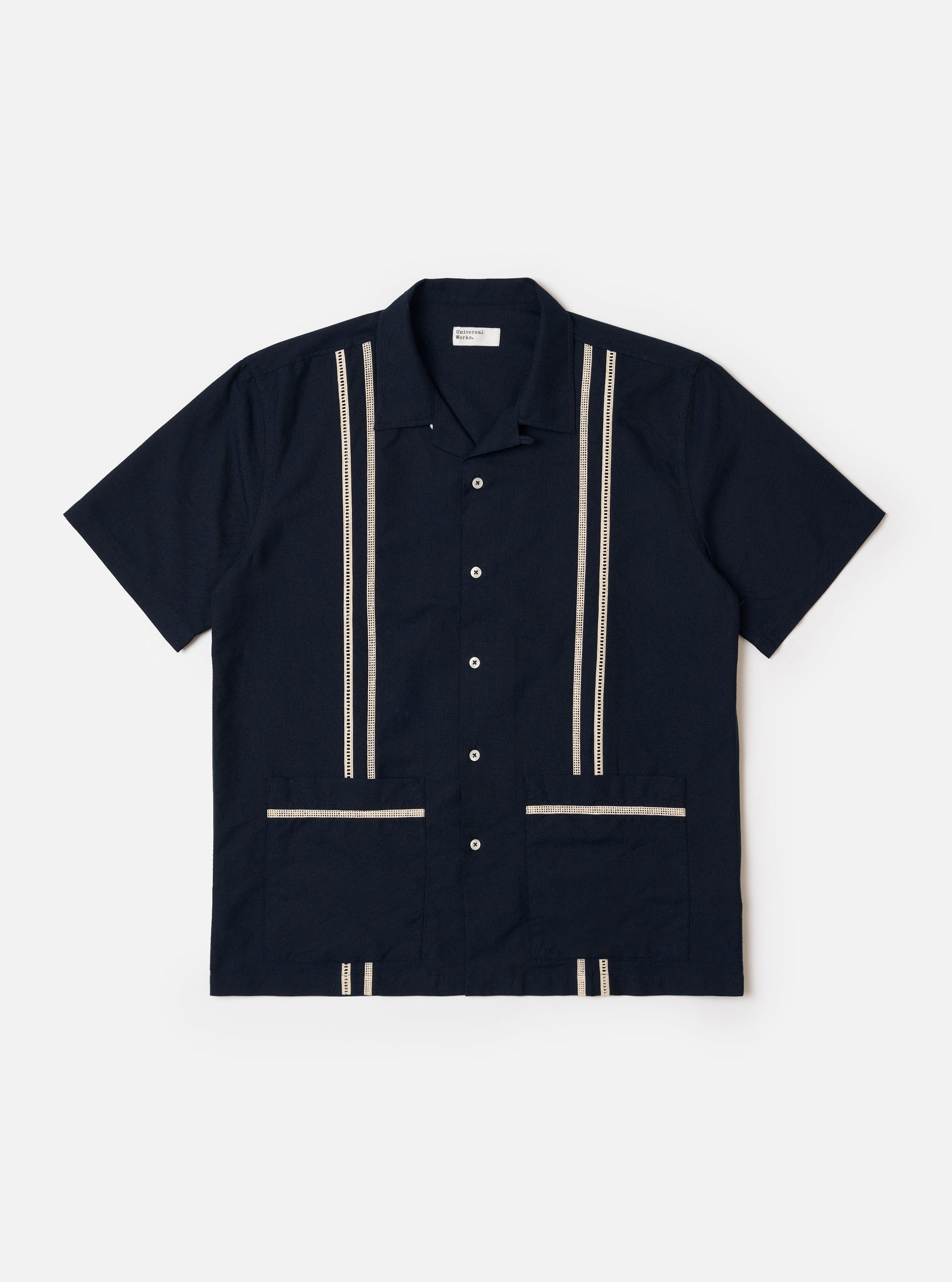 The Navy Classic Oxford Tropicana Shirt is shown as a flat lay against a plain white background. The shirt features a one-piece collar, a five-button front closure, and short, loose sleeves. Two large patch pockets are prominent on the lower front, and tonal inset embroidery detail is visible. The hem includes side splits and is longer at the back.