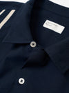 The Navy Classic Oxford Tropicana Shirt is displayed as a flat lay against a plain white background. The image shows the back of the shirt, highlighting its clean construction, simple yoke, and straight hem. The deep navy blue cotton fabric has a visible oxford weave texture.
