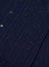 The Indigo Recycled Herringbone Bakers Overshirt is shown from the back as a flat lay against a plain white background. The image highlights the garment's textured indigo blue herringbone weave, a simple one-piece back panel, and a straight hem.