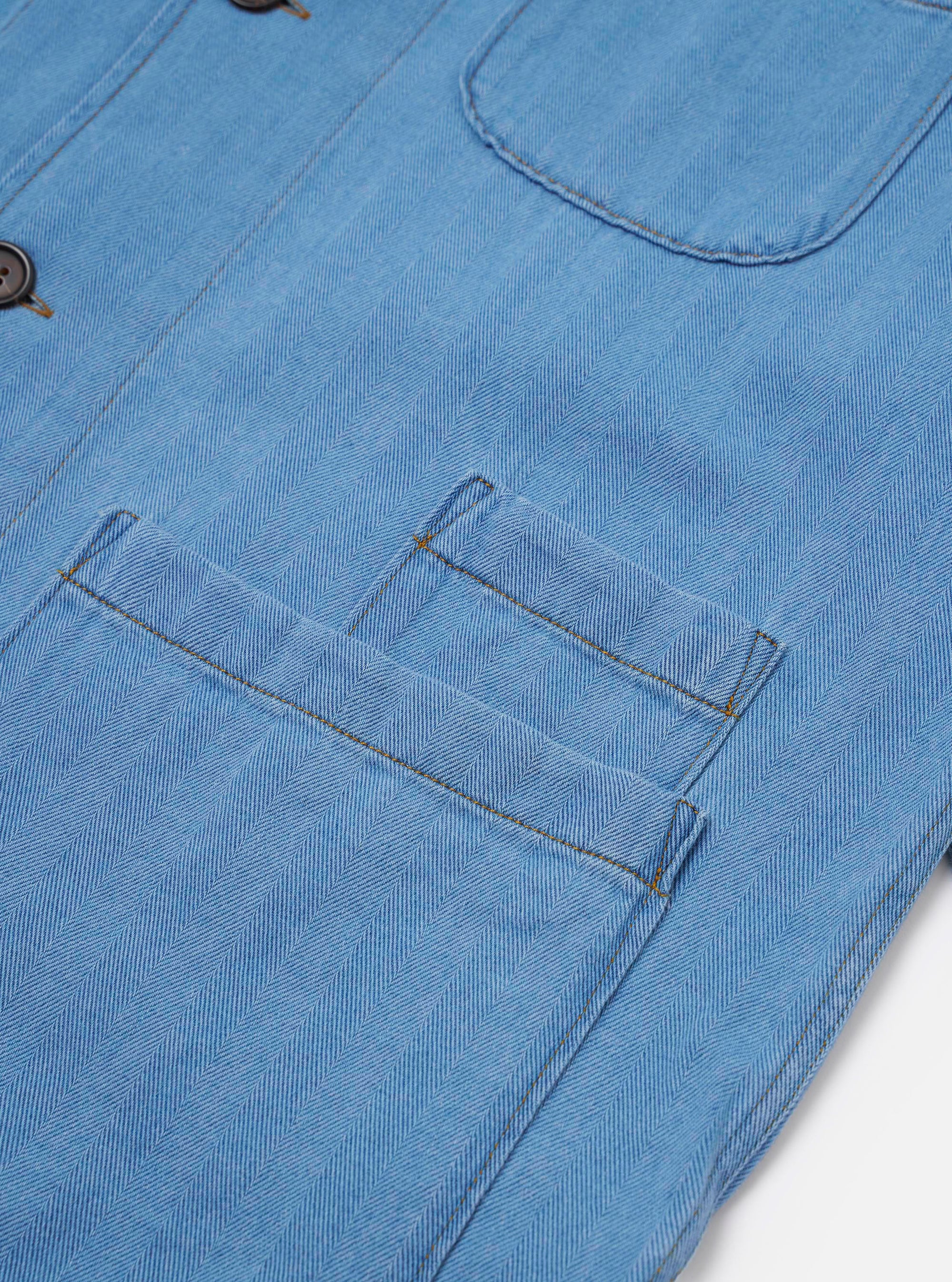 The Washed Indigo Recycled Herringbone Bakers Overshirt is shown from the back as a flat lay against a plain white background. The image highlights the straight hem, the one-piece collar, and the textured herringbone weave of the washed indigo fabric.