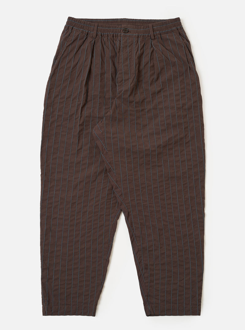The Brown Chester Stripe Pleated Track Pant is shown as a flat lay against a white background. The trousers feature an elasticated waistband with an adjustable drawstring, a single pleat at the front, and a loose, tapered leg. The cotton seersucker fabric displays a subtle vertical pinstripe pattern in brown.