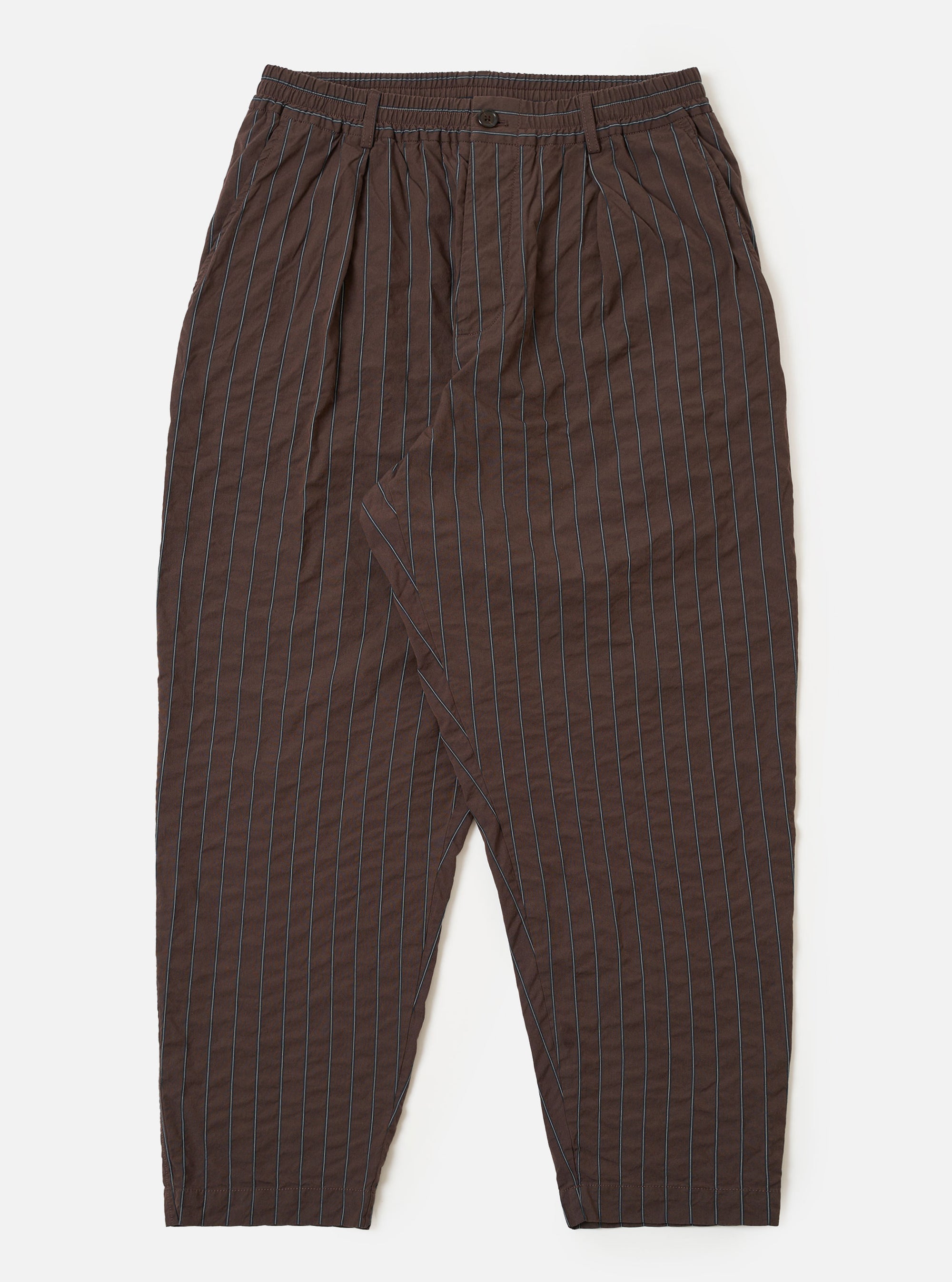 The Brown Chester Stripe Pleated Track Pant is shown as a flat lay against a white background. The trousers feature an elasticated waistband with an adjustable drawstring, a single pleat at the front, and a loose, tapered leg. The cotton seersucker fabric displays a subtle vertical pinstripe pattern in brown.