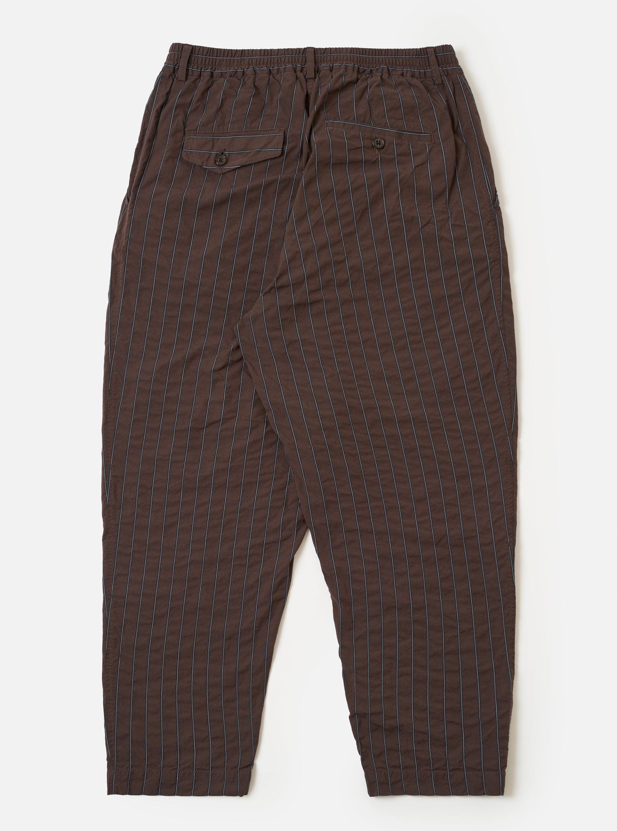 The Brown Chester Stripe Pleated Track Pant is shown from the back as a flat lay against a plain white background. The image highlights the two rear pockets—one with a buttoned flap and the other with a button jetted closure—as well as the elasticated waistband. The brown cotton fabric features a subtle pinstripe pattern and a visible seersucker texture.