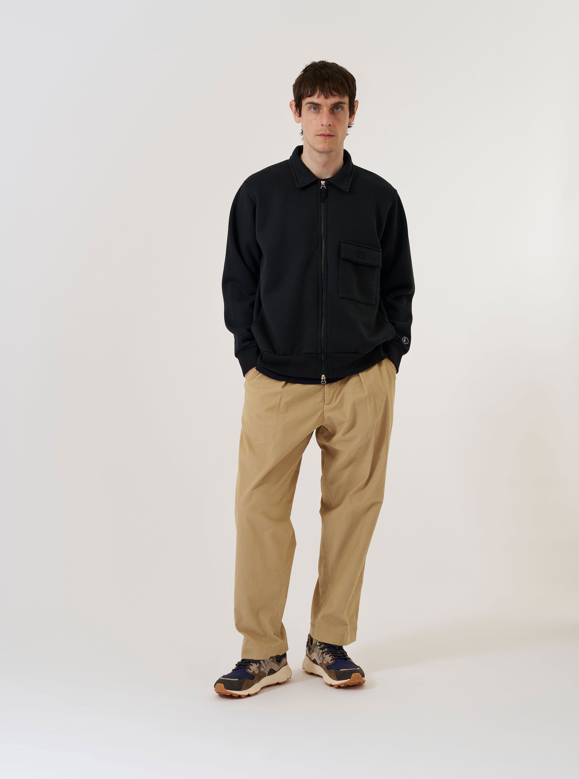 The Black Recycled Cotton Blend Jersey Tyler Jacket is shown as a flat lay against a plain white background. The jacket features a full-length two-way zip closure, a self-fabric collar, a square patch pocket with a velcro fastening on the chest, and ribbed detailing on the cuffs and hem.