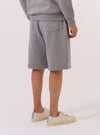 A model is wearing the Grey Marl Recycled Cotton Blend Jersey Vacation Short, shown from the waist down against a plain white background. The shorts feature a relaxed fit, an elasticated waistband, and are made from a soft, heathered grey marl jersey fabric. The model is wearing a light-colored top and white socks.