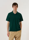 A model wears the Green Piquet Vacation Polo against a plain white background. The polo features a classic collar, a three-button placket, and a short-sleeved design with a textured piquet finish. The model is shown from the waist up, facing forward with the shirt neatly buttoned.