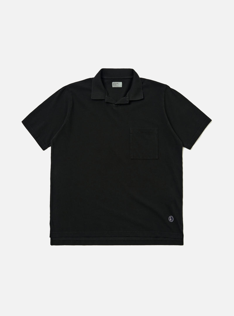 The Black Piquet Vacation Polo is shown as a flat lay against a plain white background. The polo features a single-piece open collar, a short-button placket, and a single patch pocket on the left chest. The black cotton fabric has a visible textured piquet weave.