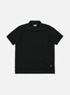 The Black Piquet Vacation Polo is shown as a flat lay against a plain white background. The polo features a single-piece open collar, a short-button placket, and a single patch pocket on the left chest. The black cotton fabric has a visible textured piquet weave.