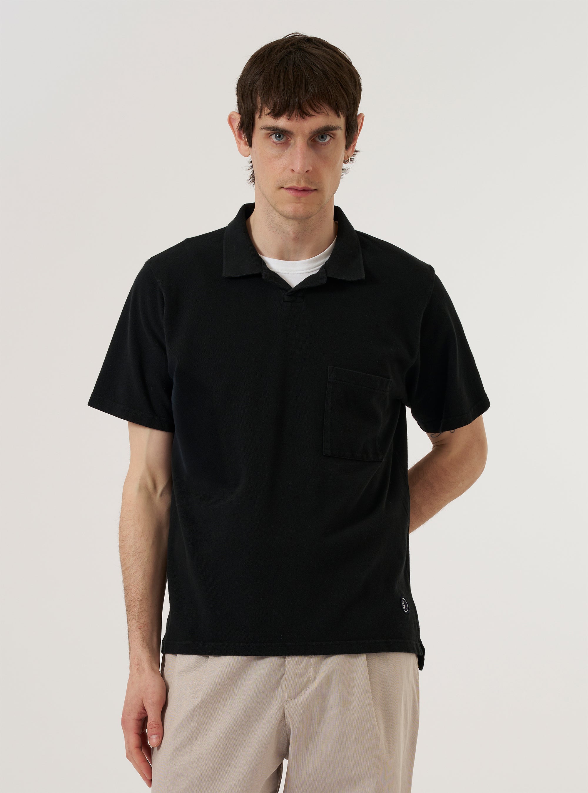 A model is wearing the Black Piquet Vacation Polo while standing against a plain white background. The polo features a classic collar, a short three-button placket, and short sleeves. The textured piquet fabric is clearly visible, and the model has the shirt untucked.
