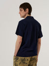 A model wears the Bright Navy Piquet Vacation Polo while standing against a plain white background. The polo features a classic collar, a short three-button placket, and short sleeves. The bright navy cotton piquet fabric has a distinct textured appearance. The model is shown from the waist up, facing forward.