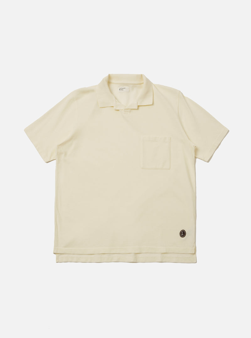 The Ecru Piquet Vacation Polo is shown as a flat lay against a white background. The polo features a one-piece open collar, a single chest patch pocket on the left side, and short sleeves. The fabric has a distinct textured piqué weave in a solid ecru color.