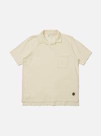 The Ecru Piquet Vacation Polo is shown as a flat lay against a white background. The polo features a one-piece open collar, a single chest patch pocket on the left side, and short sleeves. The fabric has a distinct textured piqué weave in a solid ecru color.