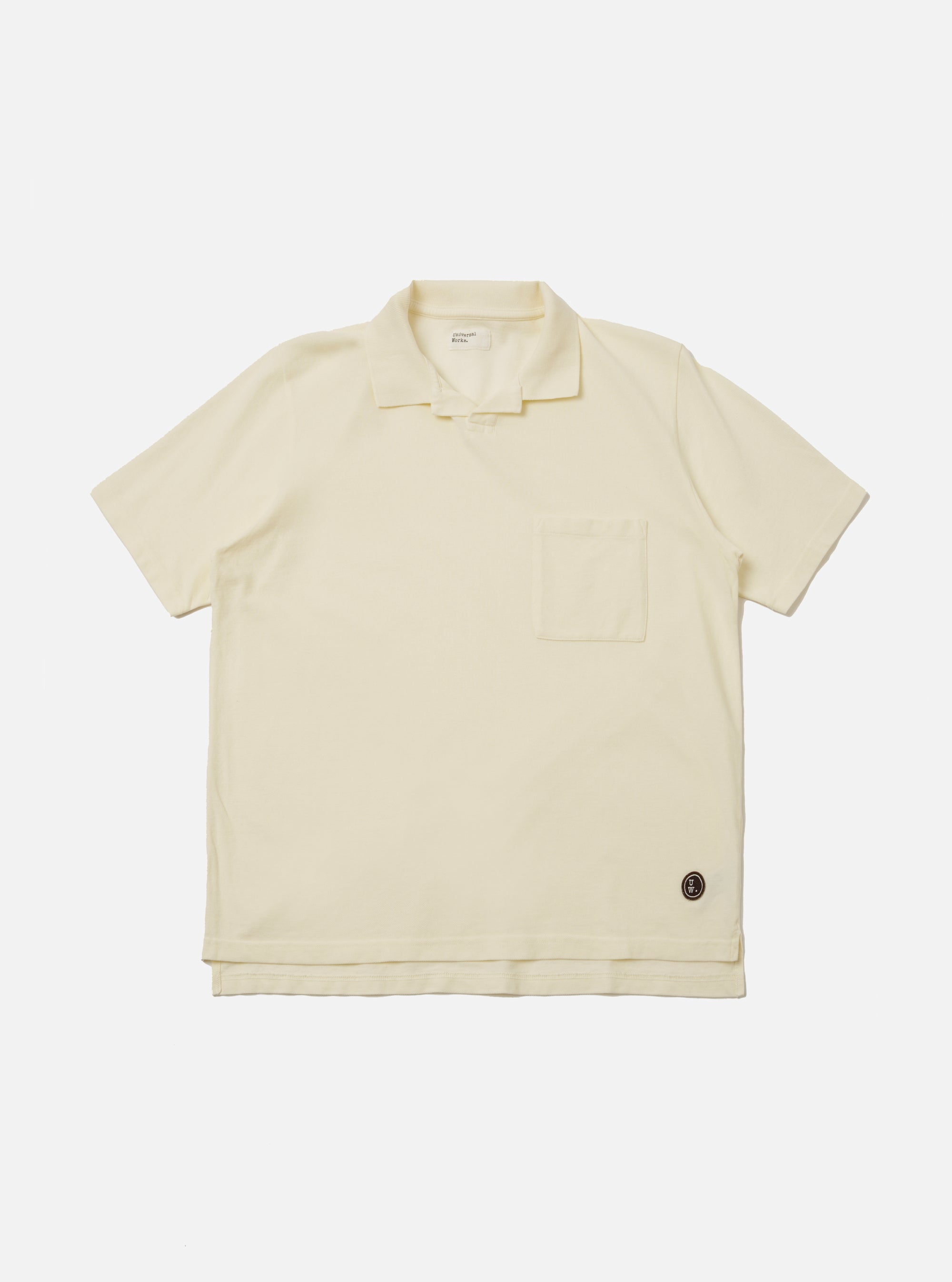 The Ecru Piquet Vacation Polo is shown as a flat lay against a white background. The polo features a one-piece open collar, a single chest patch pocket on the left side, and short sleeves. The fabric has a distinct textured piqué weave in a solid ecru color.