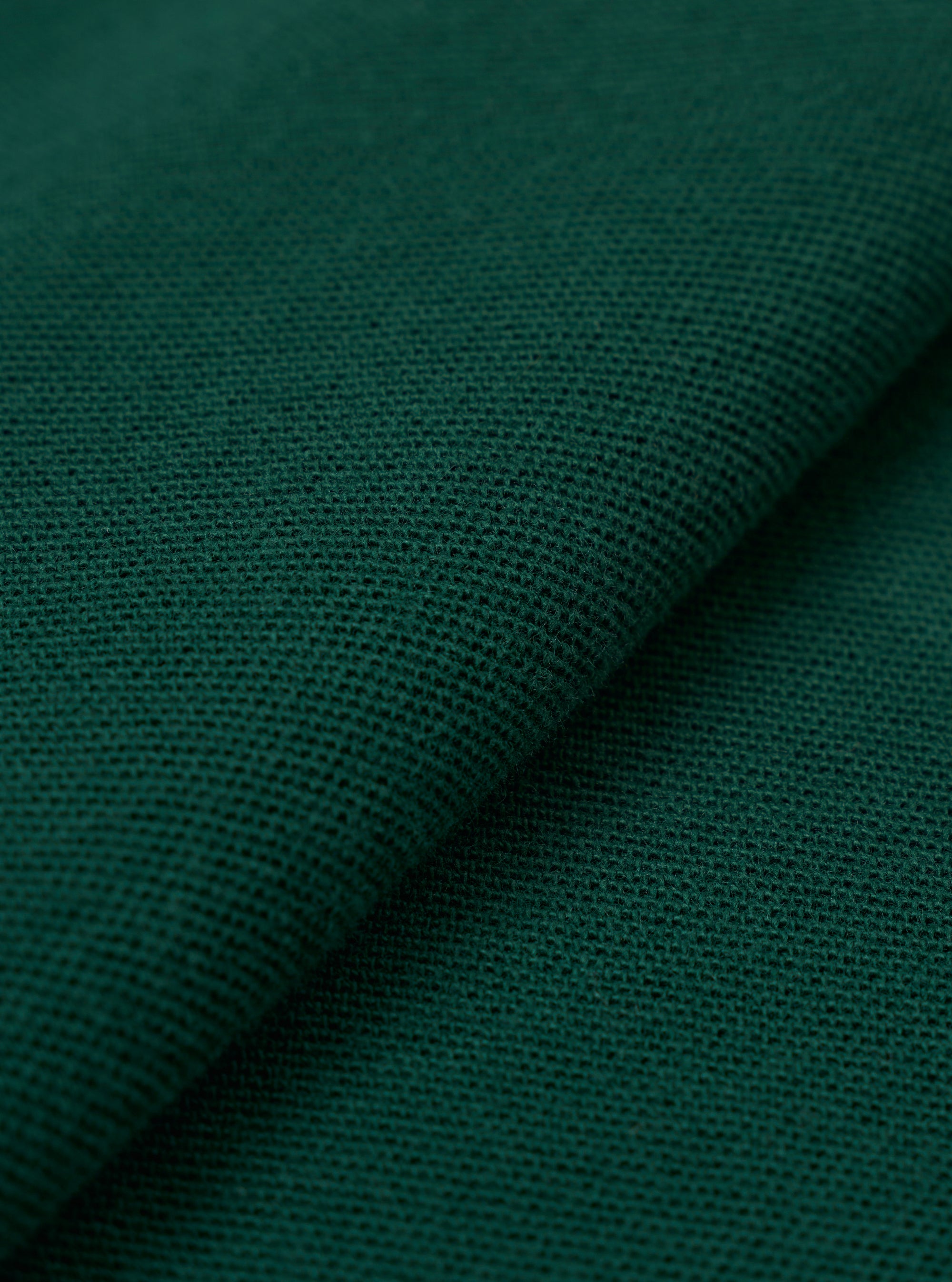 A close-up fabric swatch of the Green Piquet Vacation Polo highlights the textured, breathable weave of the green piquet fabric. The image provides a detailed view of the garment's color and knit construction.