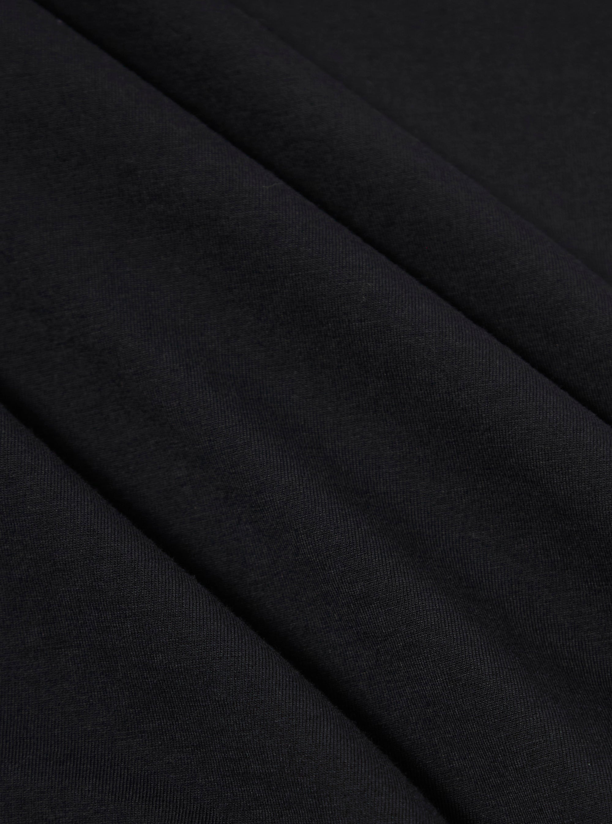 A close-up swatch image of the Black Organic Jersey Print Pocket Tee fabric highlights the solid black color and the soft, smooth texture of the organic cotton jersey. The image provides a detailed view of the knit material.