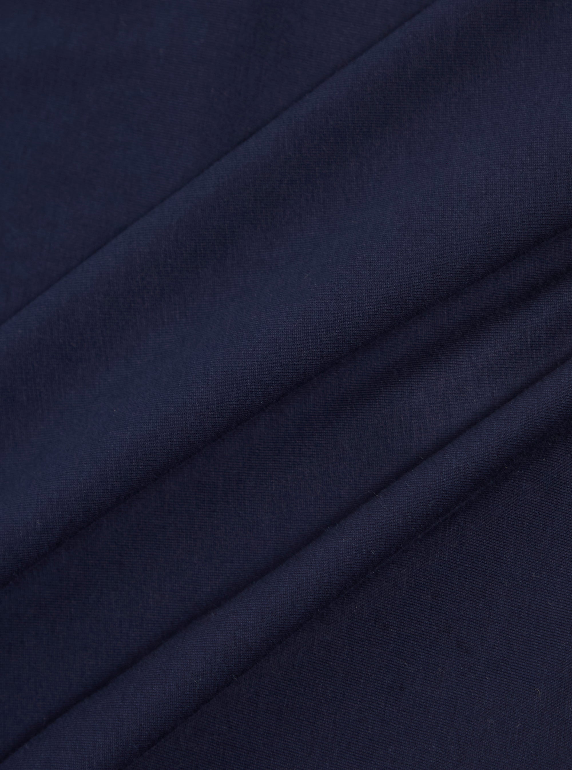 A close-up swatch image of the Bright Navy Organic Jersey Print Pocket Tee fabric highlights the vibrant navy blue color and the soft, fine-knit texture of the organic cotton jersey. The material fills the entire frame, providing a detailed view of the garment's color and construction.