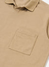 The Sand Rugby Jersey Oversized Vacation Polo is shown from the back as a flat lay against a white background. The image highlights the stepped hem, where the back of the polo is longer than the front, and the small side vents. The sand-colored organic cotton fabric has a smooth, jersey texture.