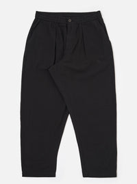 The Black Merida Seersucker Pleated Track Pant is shown as a flat lay against a white background. The trousers feature an elasticated waistband with a central drawstring, a single pleat on each leg, and two side pockets. The black cotton fabric has a distinct puckered seersucker texture.