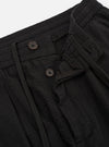The Black Merida Seersucker Pleated Track Pant is shown from a rear three-quarter angle as a flat lay against a plain white background. The image highlights the elasticated waistband and the two rear pockets, consisting of one buttoned flap pocket and one button-jetted pocket. The black cotton fabric features a visible puckered seersucker texture and diagonal stitching details.