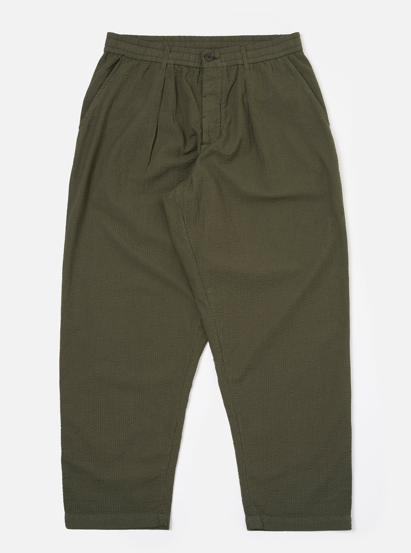 The Olive Merida Seersucker Pleated Track Pant is shown as a flat lay against a plain white background. The image highlights the elasticated waistband with an external drawstring, the single pleat at the front, and the tapered leg design. The olive green cotton fabric features a distinct puckered seersucker texture with a subtle checkered pattern.