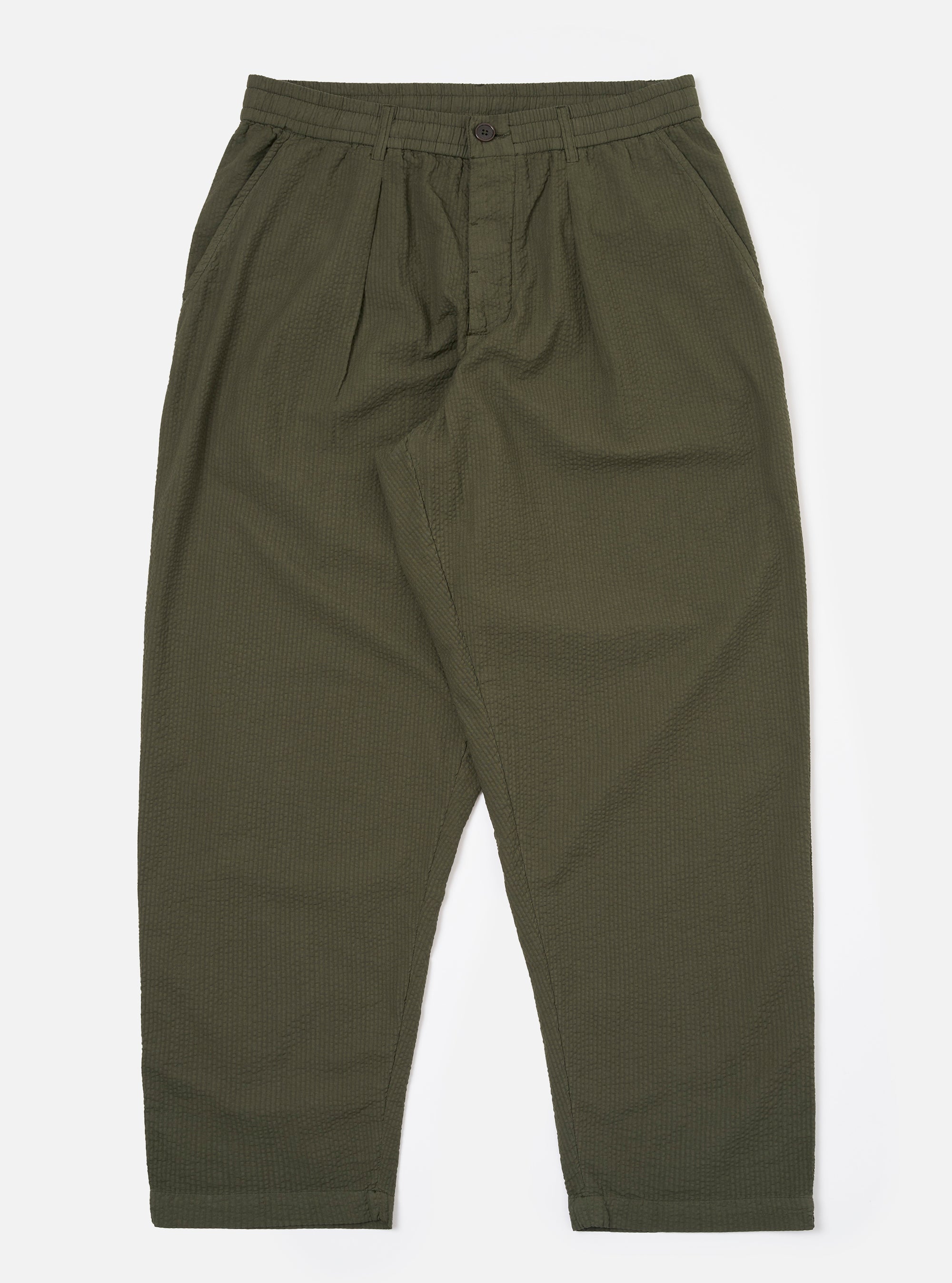 The Olive Merida Seersucker Pleated Track Pant is shown as a flat lay against a plain white background. The image highlights the elasticated waistband with an external drawstring, the single pleat at the front, and the tapered leg design. The olive green cotton fabric features a distinct puckered seersucker texture with a subtle checkered pattern.