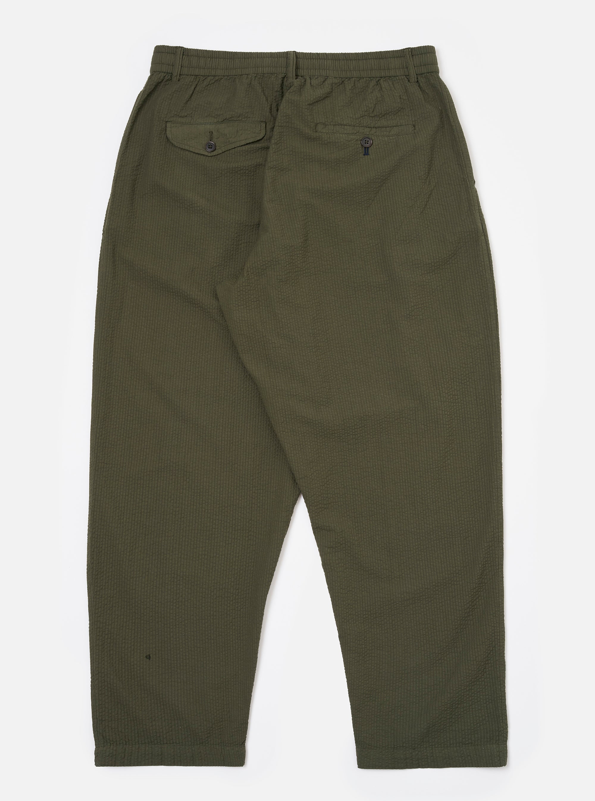 The Olive Merida Seersucker Pleated Track Pant is shown from the back as a flat lay against a plain white background. The image highlights the two rear pockets, including one with a buttoned flap and one button jetted pocket, and the elasticated waistband. The olive green cotton fabric features a visible seersucker texture.