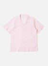 The Pink Lily Stripe Road Shirt is shown as a flat lay against a white background. The short-sleeve shirt features a pink and white vertical pinstripe pattern, a single chest patch pocket on the left side, and a straight hem. The camp collar is open-necked with a visible loop closure at the top. The fabric has a fine seersucker texture.