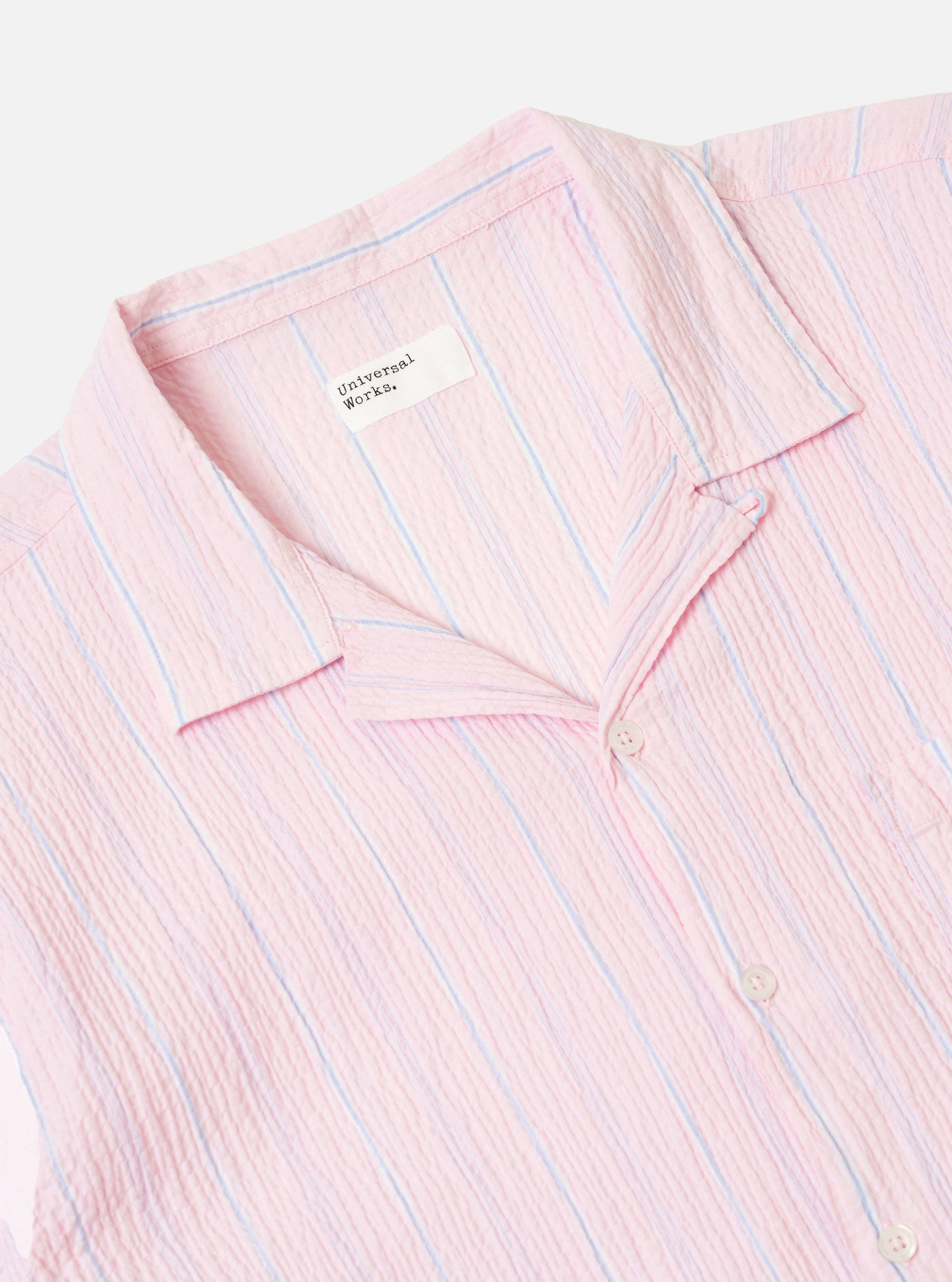 The Pink Lily Stripe Road Shirt is shown from the back as a flat lay against a white background. The shirt features vertical stripes in pink and white, a straight hem, and a back yoke with a central box pleat. The short sleeves are visible, and
